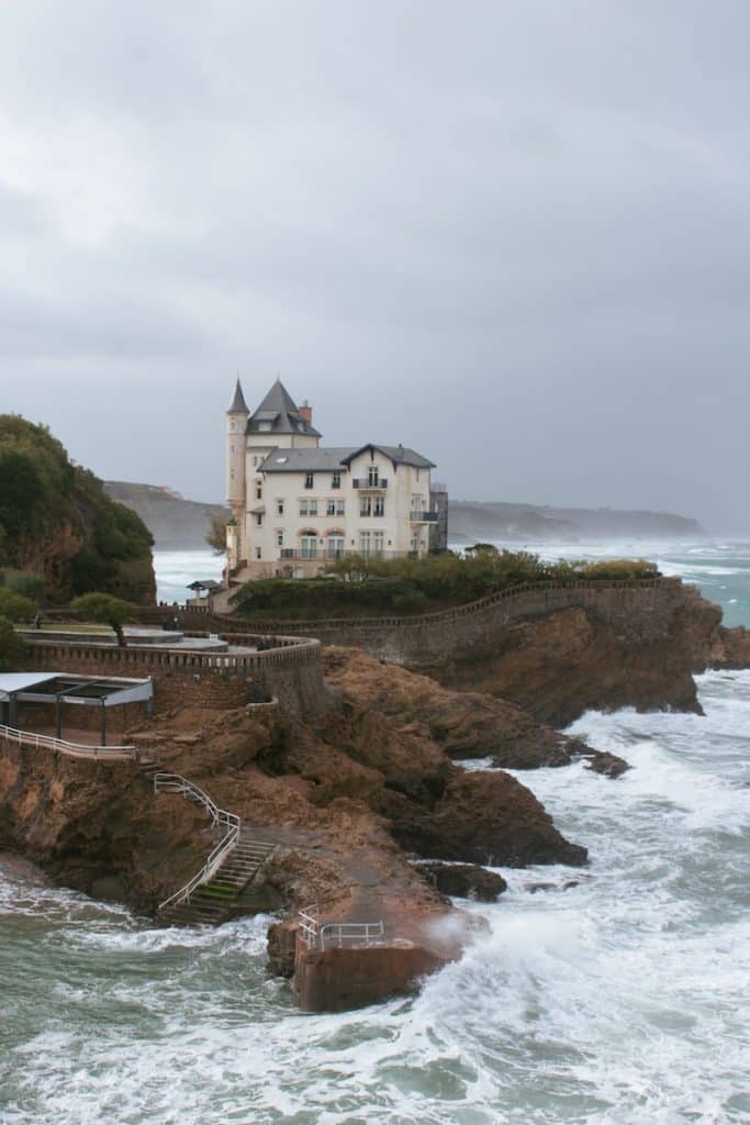 a large white house sitting on top of a cliff next to the ocean